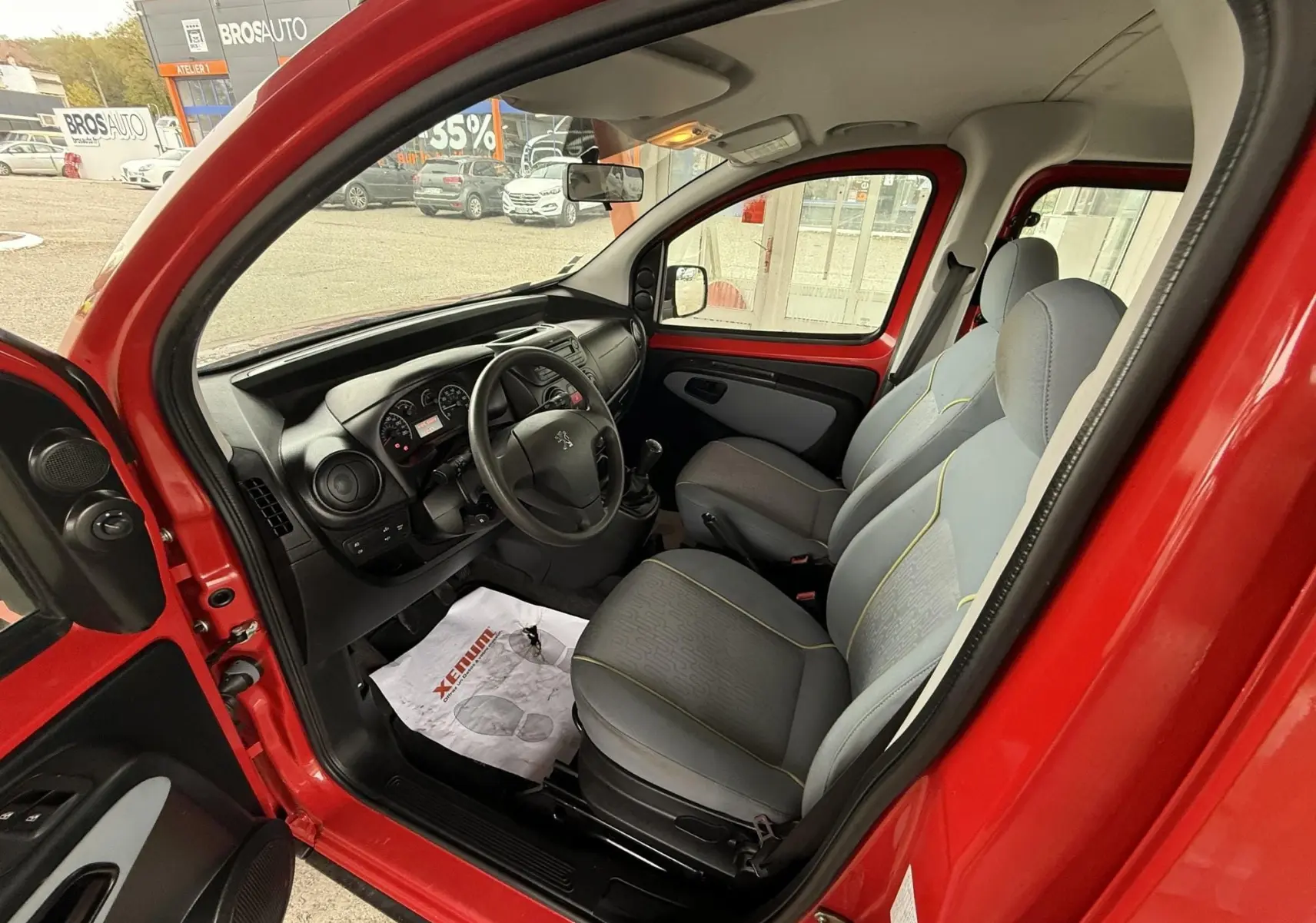 Vue intérieure côté gauche du Peugeot Bipper Tepee rouge, montrant les sièges tissu gris et le tableau de bord noir.