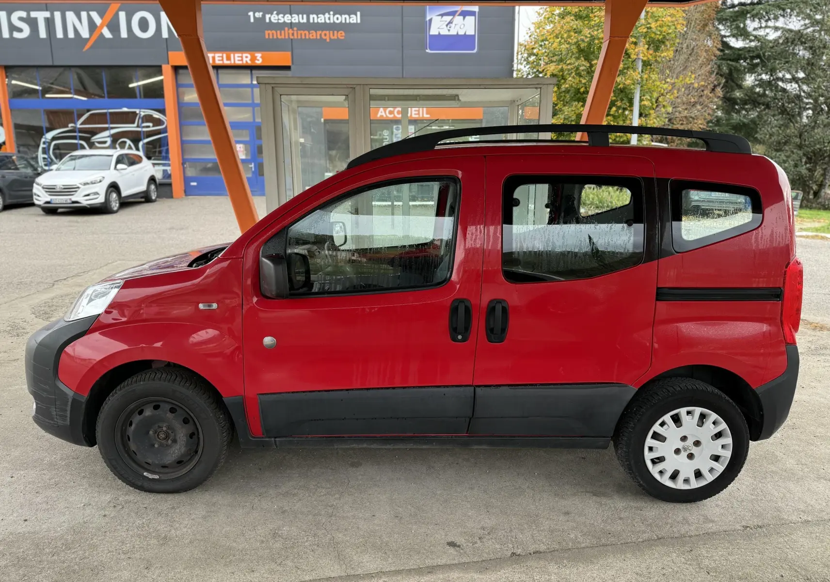 Profil gauche d'un Peugeot Bipper Tepee rouge 2013 avec portes coulissantes et jantes différentes à l'avant et arrière.