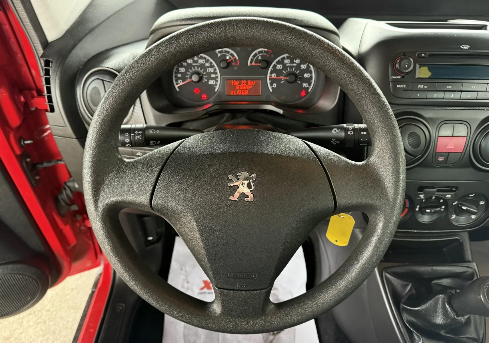 Vue intérieure centrée sur le volant Peugeot d'un Bipper Tepee rouge, avec tableau de bord et console radio visibles.