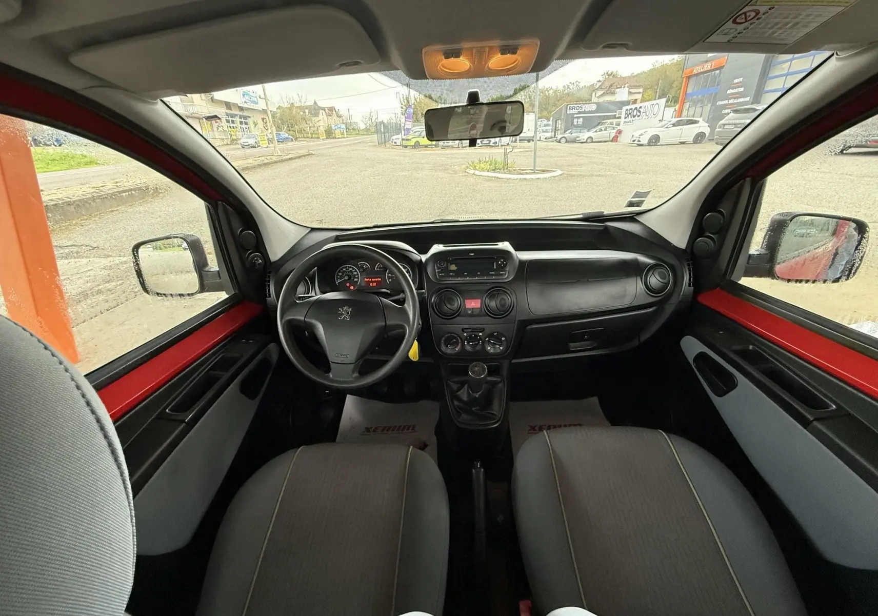 Vue intérieure avant du Peugeot Bipper Tepee rouge de 2013, montrant le tableau de bord et les sièges tissu gris.