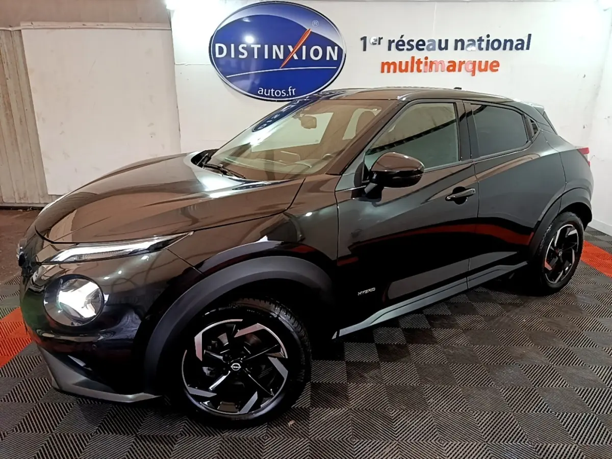 Nissan Juke Hybrid 143 Business+ noir vu de 3/4 avant droit, avec jantes noires et logo Distinxion en arrière-plan.
