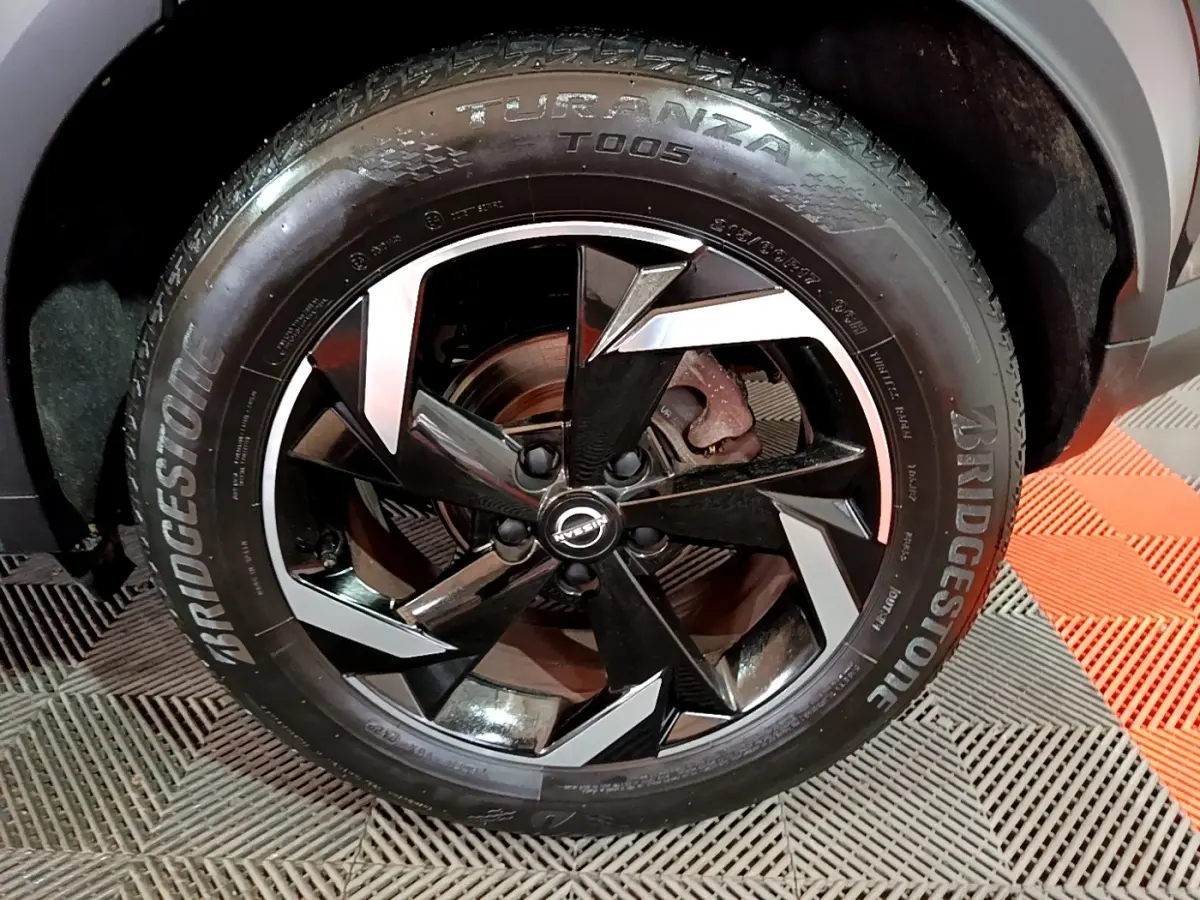Gros plan sur la roue avant gauche du Nissan Juke Hybrid 143 Business+ noir avec jante alliage bicolore et pneu Bridgestone.