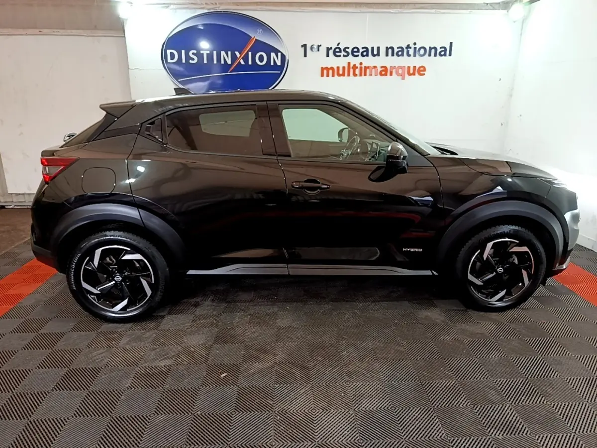 Profil droit d'un Nissan Juke Hybrid 143 Business+ noir, avec jantes noires et logo Hybrid visible sur la porte avant.