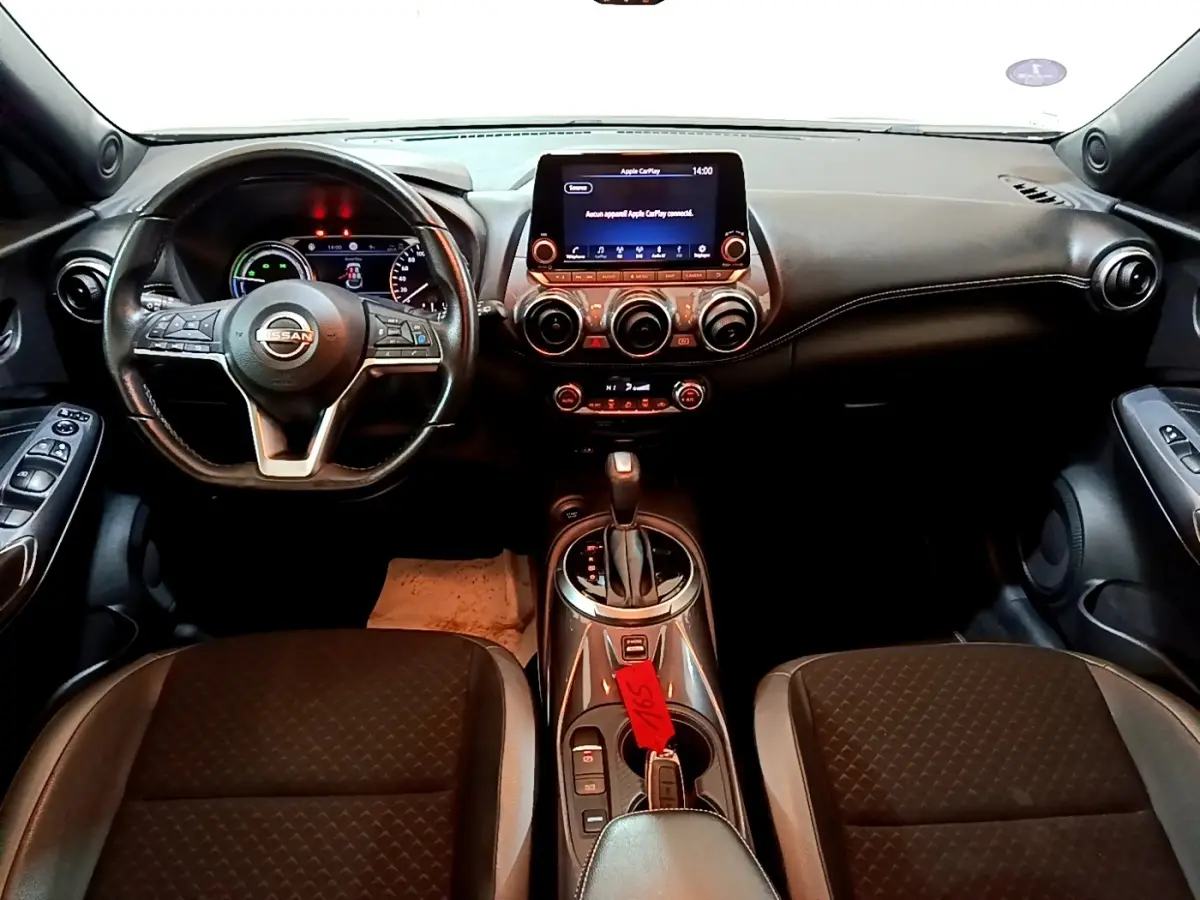 Vue intérieure frontale du tableau de bord et volant cuir noir du Nissan Juke Hybrid 2022 avec écran tactile central allumé.