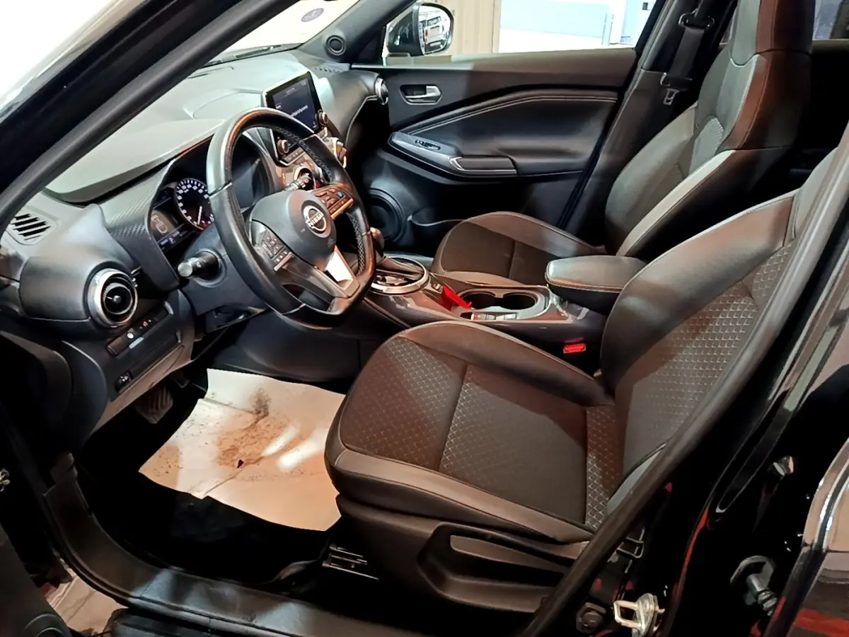 Vue intérieure côté conducteur du Nissan Juke Hybrid 143 Business+ noir, avec tableau de bord et sièges avant en tissu noir.