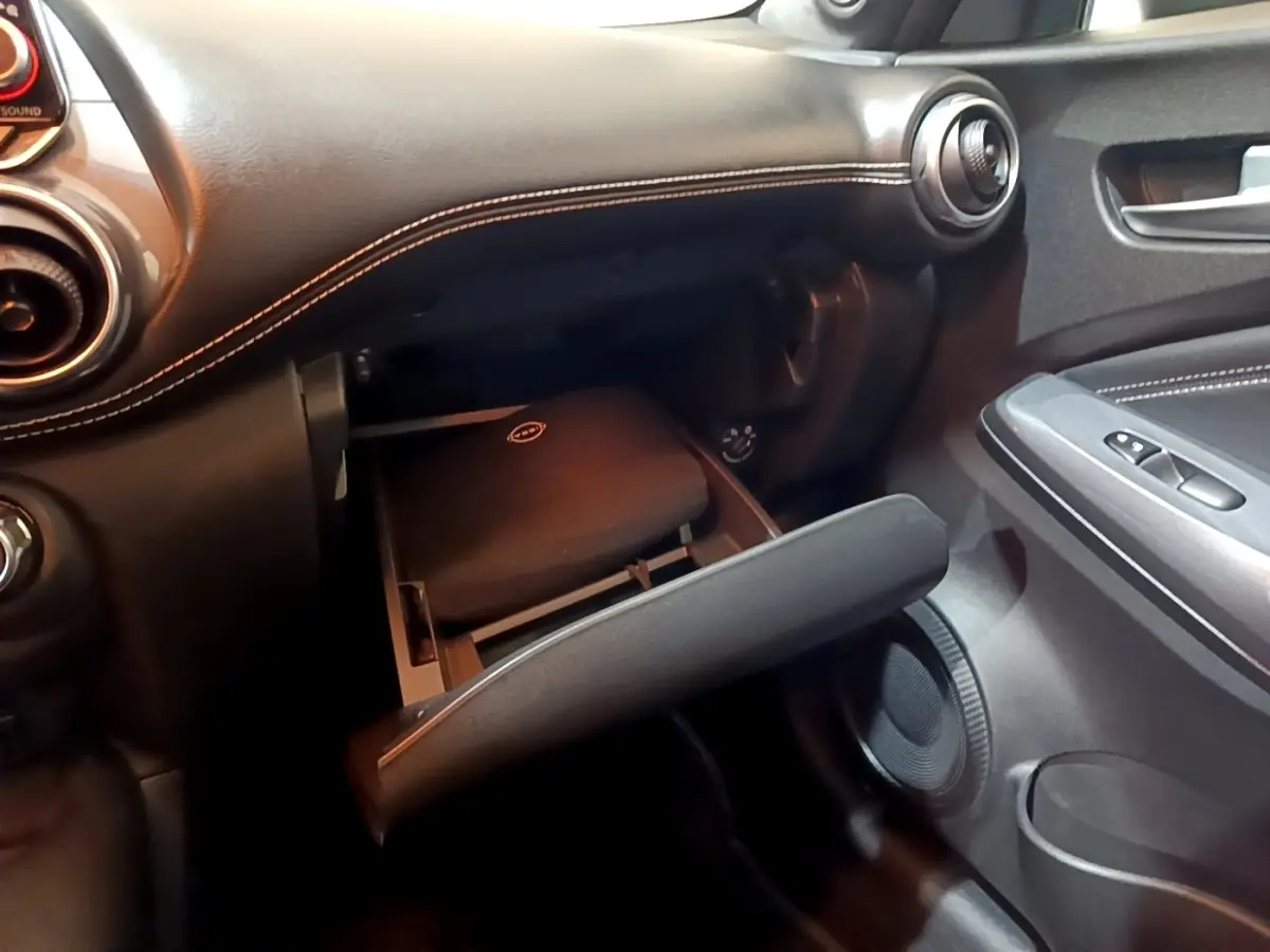 Intérieur noir du Nissan Juke Hybrid 2022, vue côté passager sur la boîte à gants ouverte avec coutures blanches visibles.