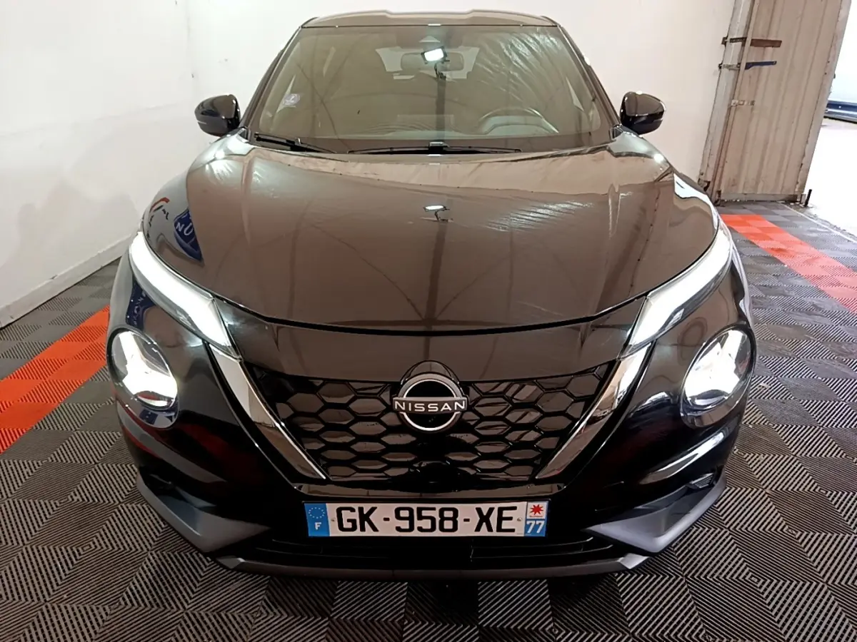 Vue avant d'un Nissan Juke Hybrid 143 Business+ noir avec calandre en nid d'abeille et phares allumés.