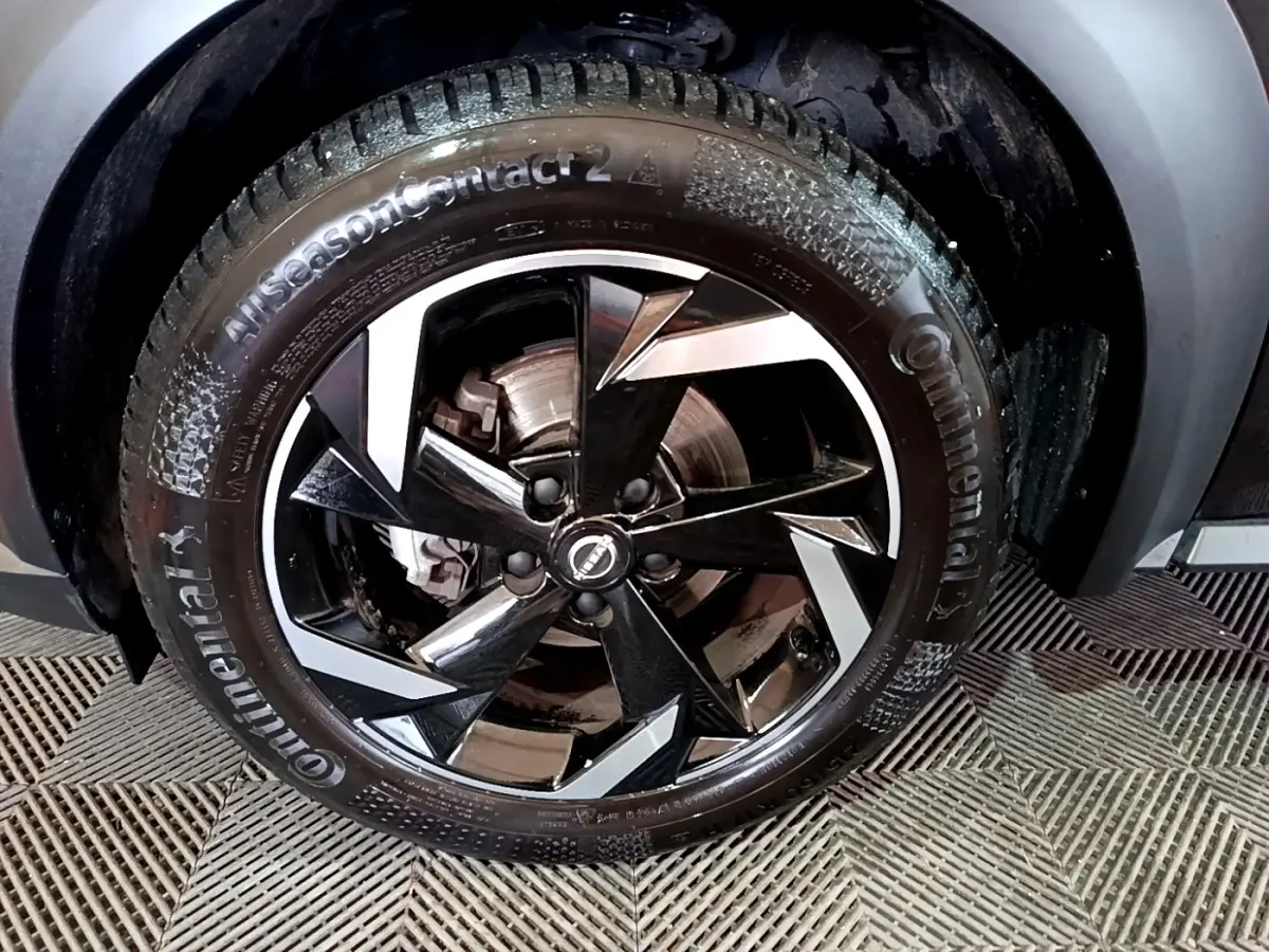 Gros plan sur la roue avant droite noire du Nissan Juke Hybrid 143 Business+ avec jante en alliage bicolore.