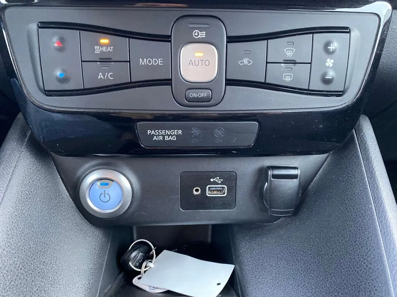 Détail de la console centrale noire de la Nissan Leaf blanche 2020, montrant les commandes de climatisation et ports USB.