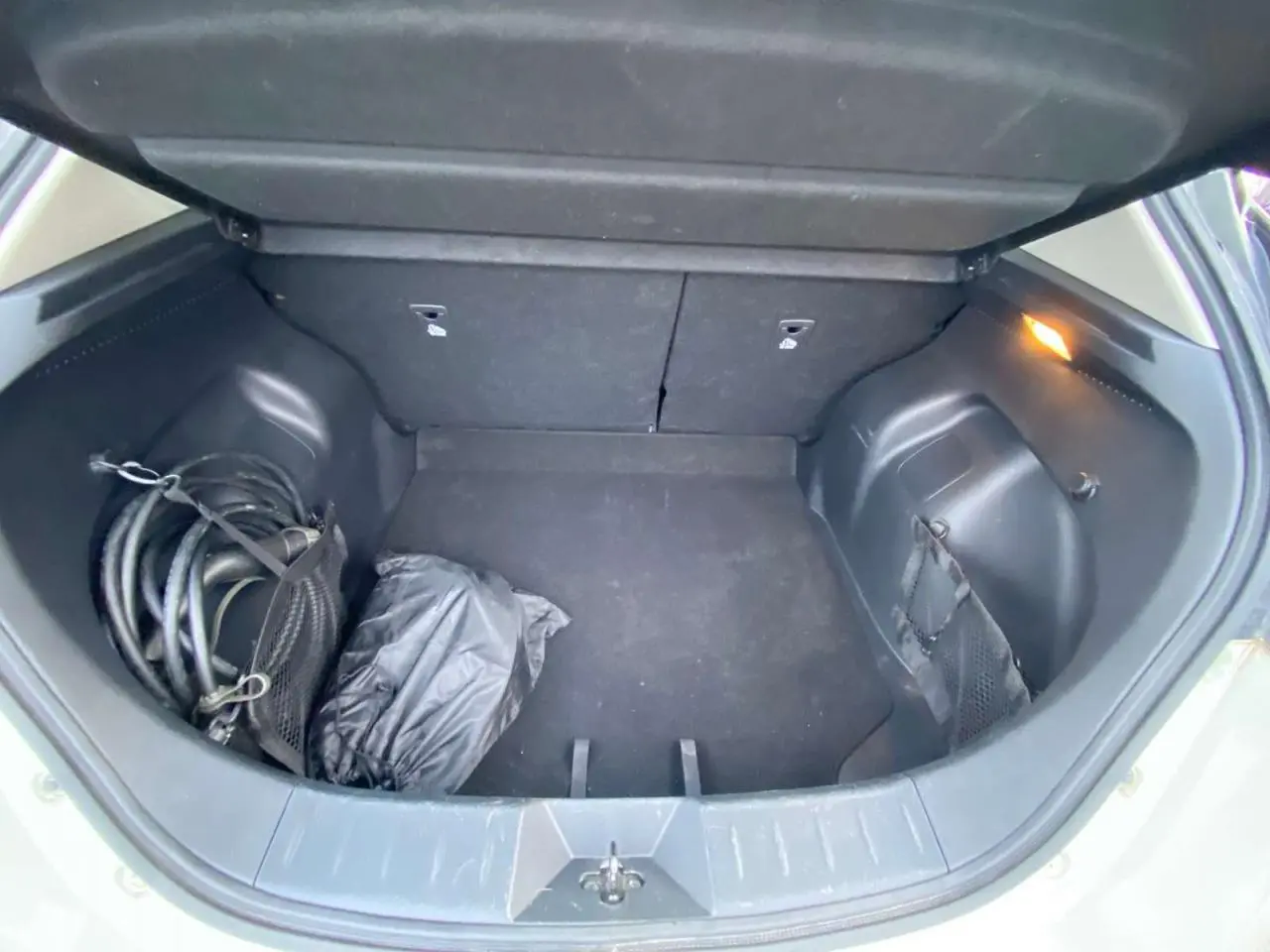 Coffre ouvert d'une Nissan Leaf blanche 2020, vue de dessus montrant un câble de recharge et un sac noir.