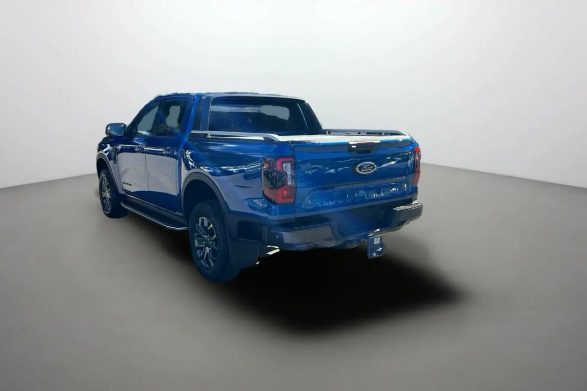 Ford Ranger 2.0 205 Wildtrak Plus bleu lightning vu en 3/4 arrière droit avec attelage et barres de toit.