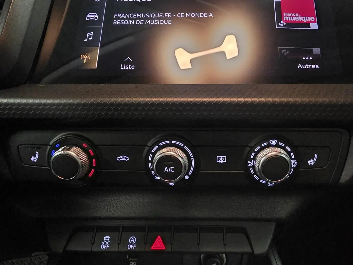 Gros plan sur la console centrale de l'Audi A1 2020, montrant les commandes de climatisation manuelle et sièges chauffants.