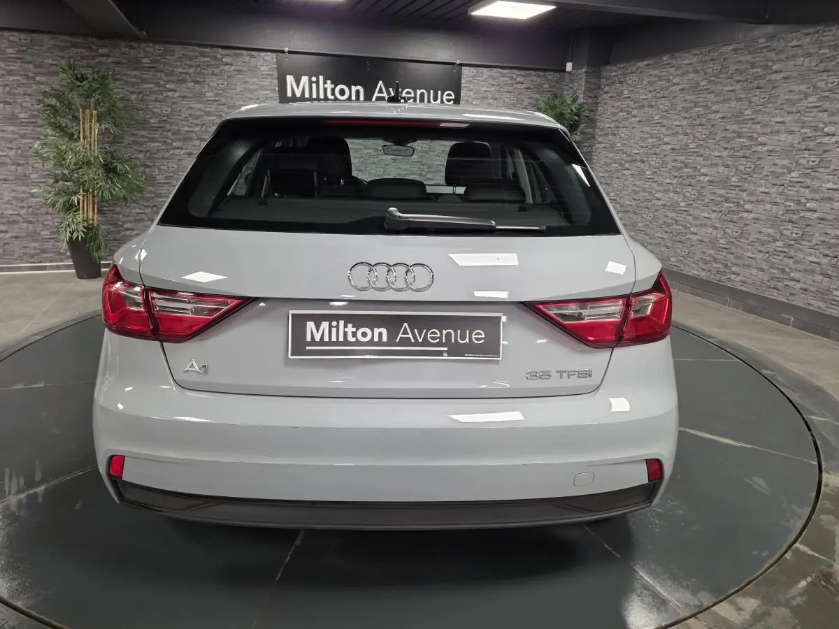 Vue arrière d'une Audi A1 Sportback gris Manhattan avec feux LED et logo Audi visible sur un plateau tournant.