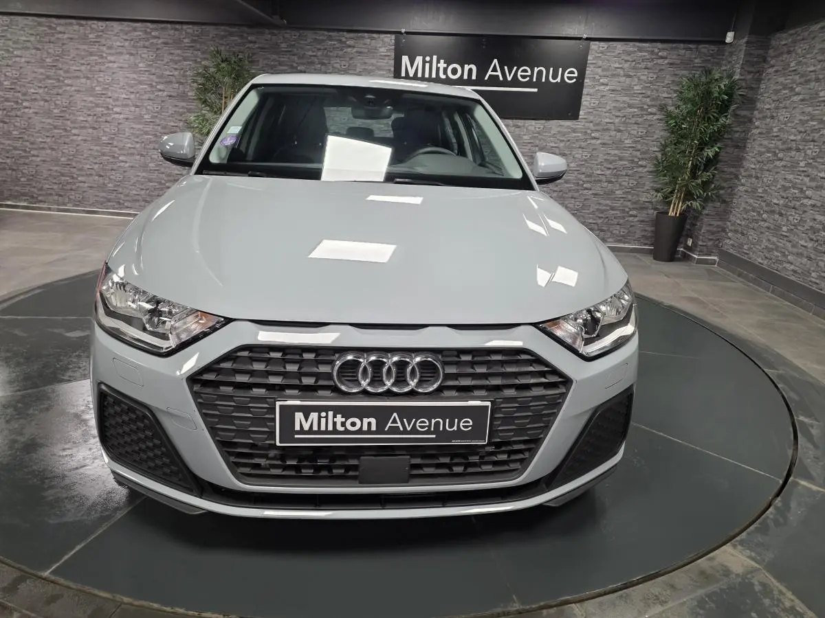 Vue frontale d'une Audi A1 Sportback gris Manhattan avec calandre noire et logo Audi visible en showroom.