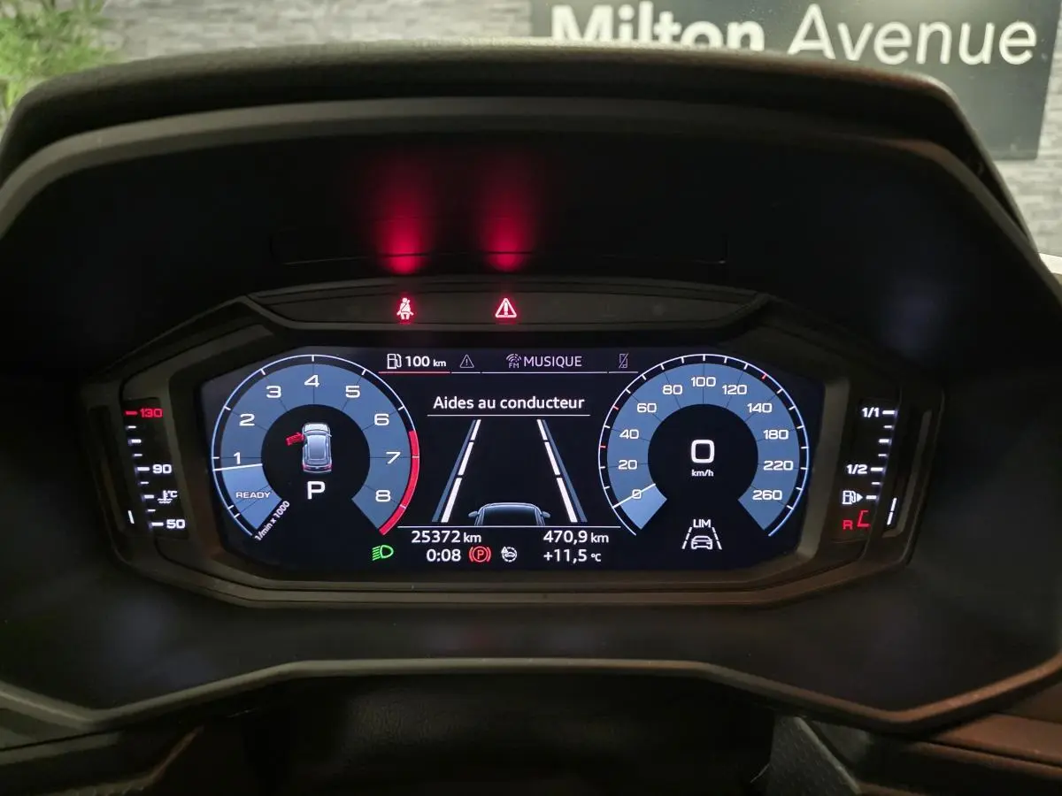 Affichage numérique du tableau de bord de l'Audi A1 Sportback gris, montrant les aides au conducteur et compteurs à 0 km/h.