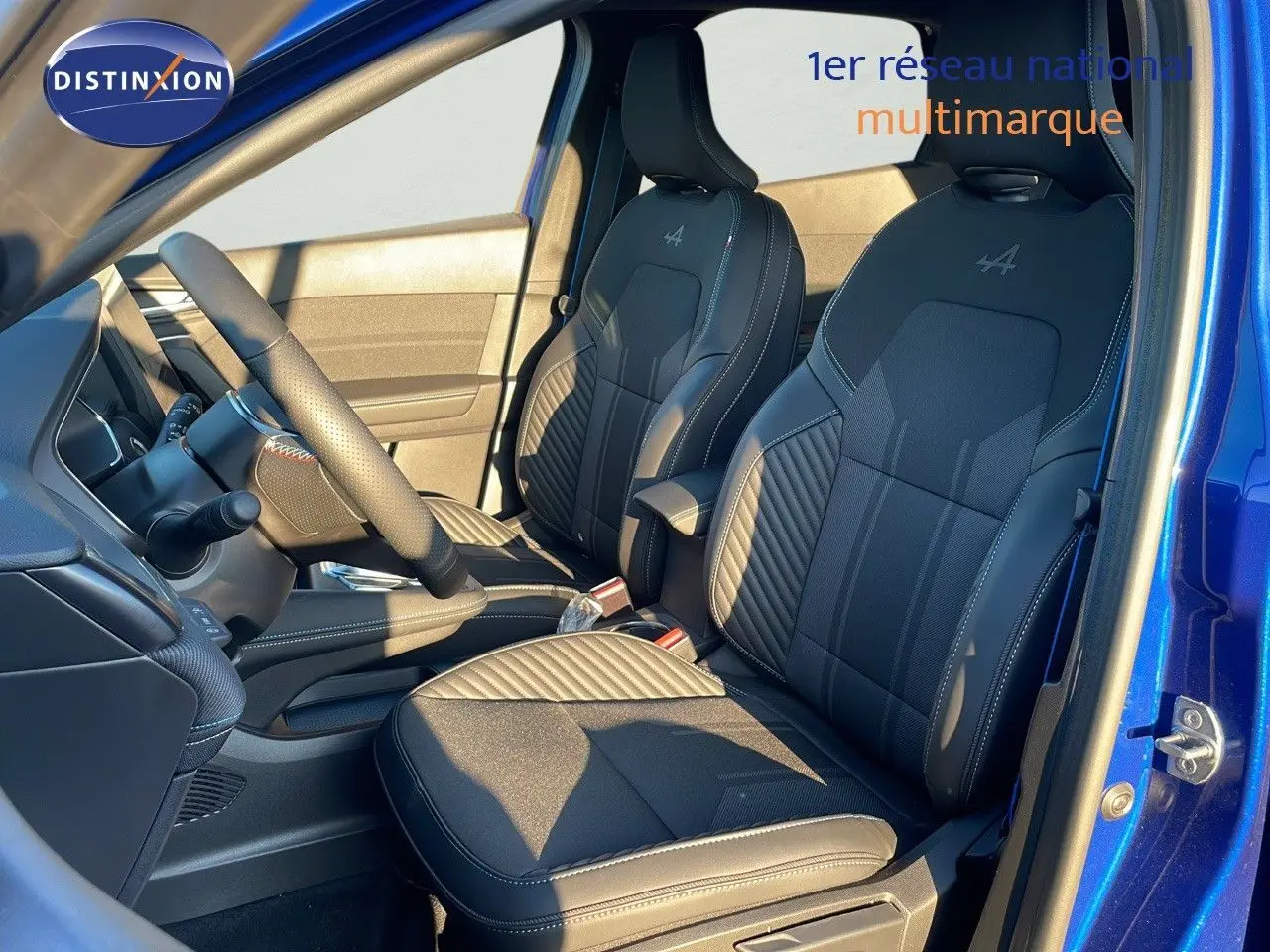 Intérieur avant du Renault Captur E-Tech hybride 2025, sièges noirs avec surpiqûres et logo Alpine, porte ouverte bleu Iron Metal.