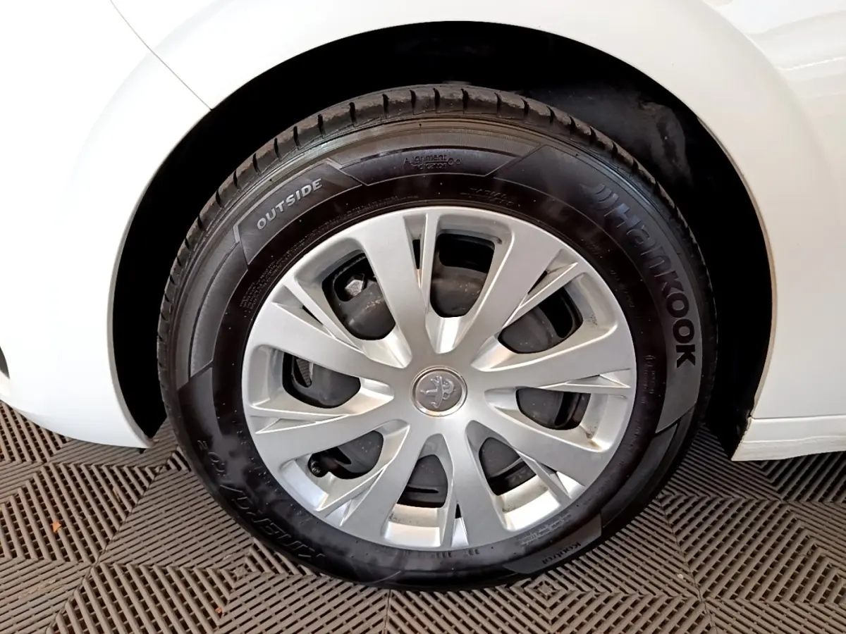 Gros plan sur la roue avant droite d'une Peugeot 208 blanche, mettant en valeur la jante et le pneu Hankook.