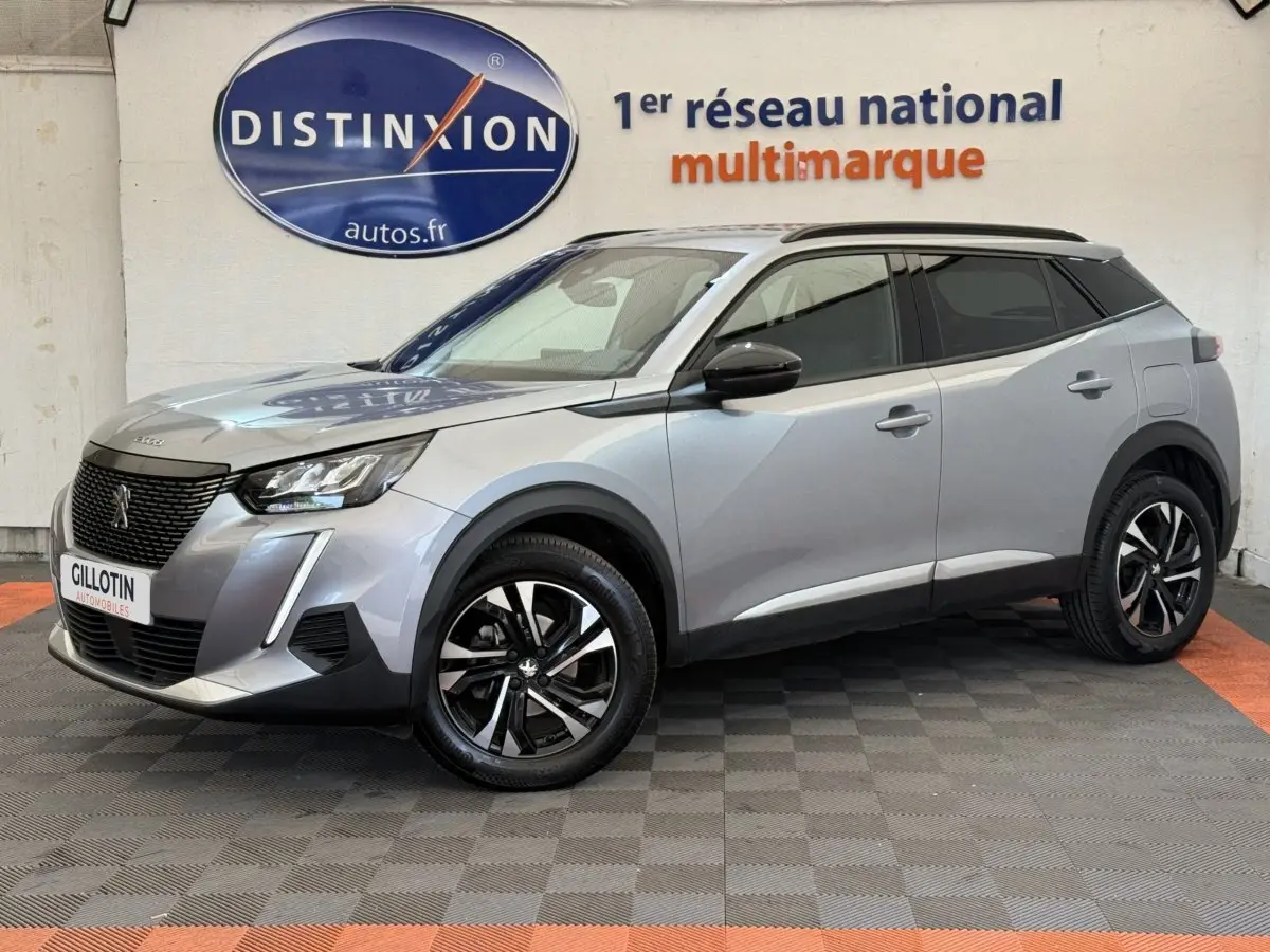 Peugeot 2008 gris clair en 3/4 avant droit, avec jantes noires et toit noir contrasté visible en intérieur showroom.