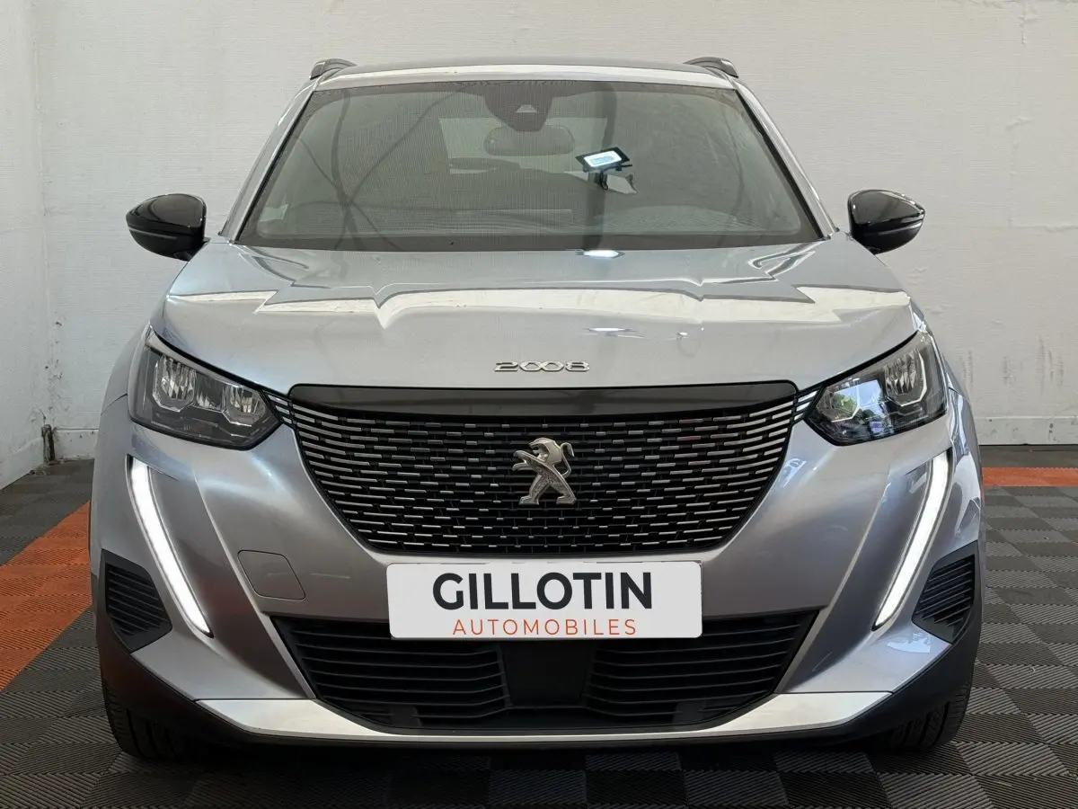 Vue frontale d'un Peugeot 2008 gris clair avec calandre noire et feux LED verticaux allumés.
