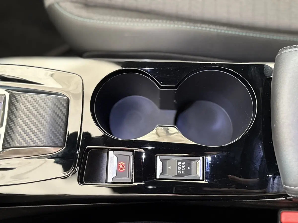 Gros plan sur la console centrale noire brillante du Peugeot 2008 gris clair, avec porte-gobelets et commandes Drive Mode et frein à main électrique.