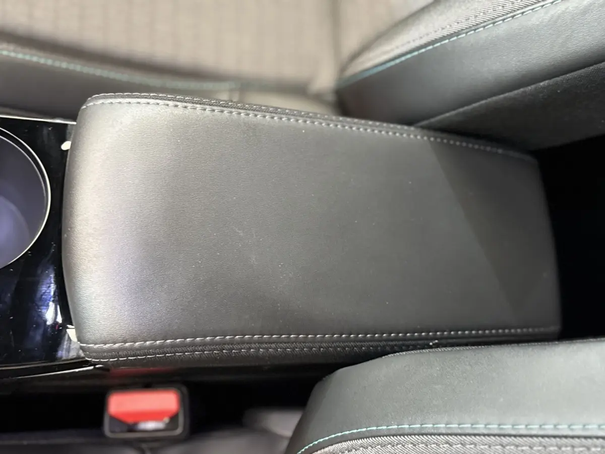 Gros plan sur l'accoudoir central en cuir noir avec surpiqûres bleues dans l'habitacle du Peugeot 2008 gris clair.