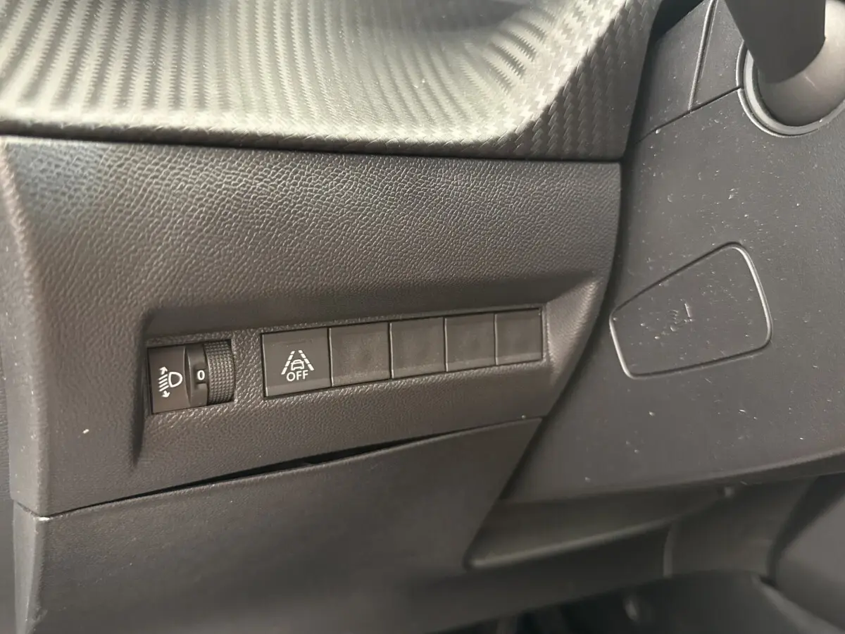 Détail intérieur côté gauche du tableau de bord noir avec commandes de réglage des phares et d'alerte de franchissement de ligne.