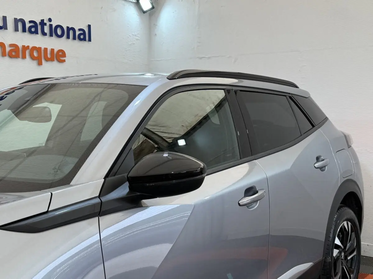 Vue de côté droit 3/4 arrière d’un Peugeot 2008 gris clair avec rétroviseur noir et toit noir contrasté.