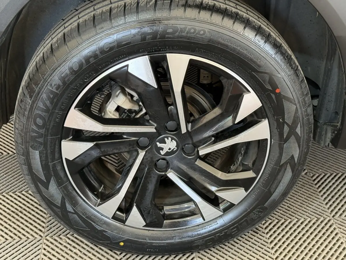 Gros plan sur la jante alliage noire et argentée avec logo Peugeot au centre, montée sur un pneu neuf.