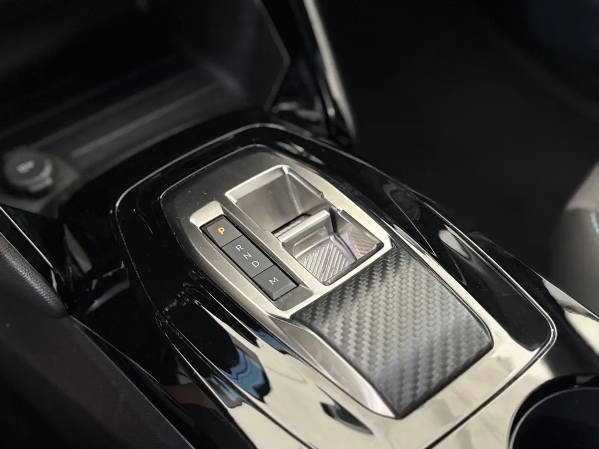 Gros plan sur la console centrale noire brillante avec sélecteur de boîte auto et finition carbone dans un Peugeot 2008 gris clair.