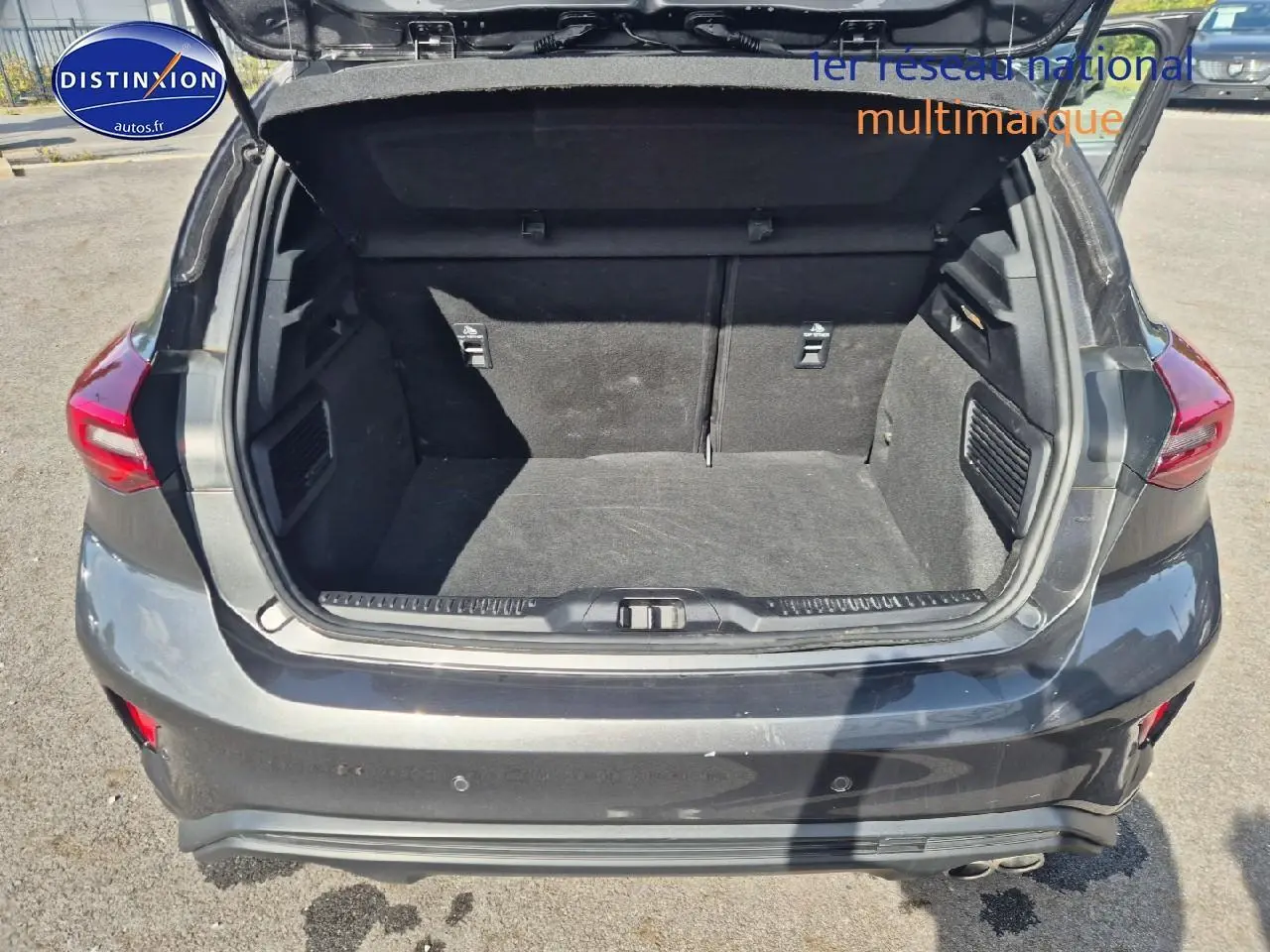 Coffre ouvert vu de l'arrière d'une Ford Focus gris magnétique 2024 avec feux arrière LED et double sortie d'échappement.