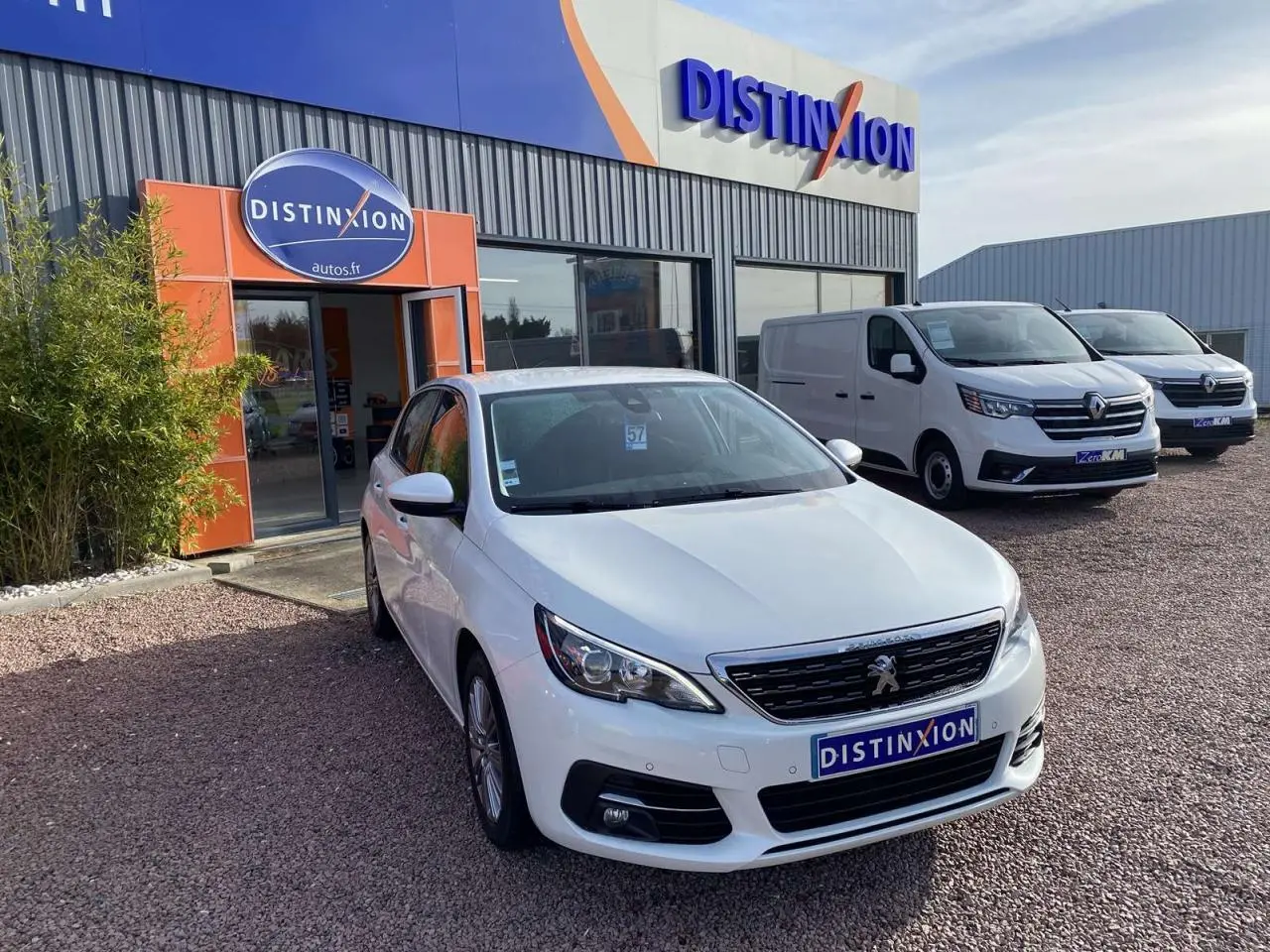 Peugeot 308 blanc nacré vue 3/4 avant droit devant un concessionnaire Distinxion par temps clair.