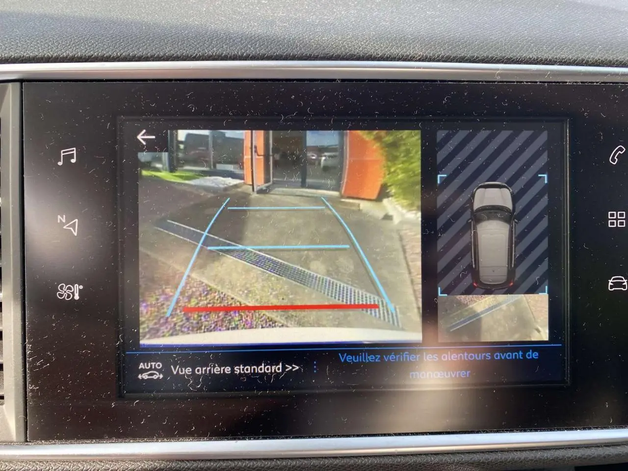 Écran tactile montrant la caméra de recul et l'aide au stationnement arrière de la Peugeot 308 blanche nacrée.