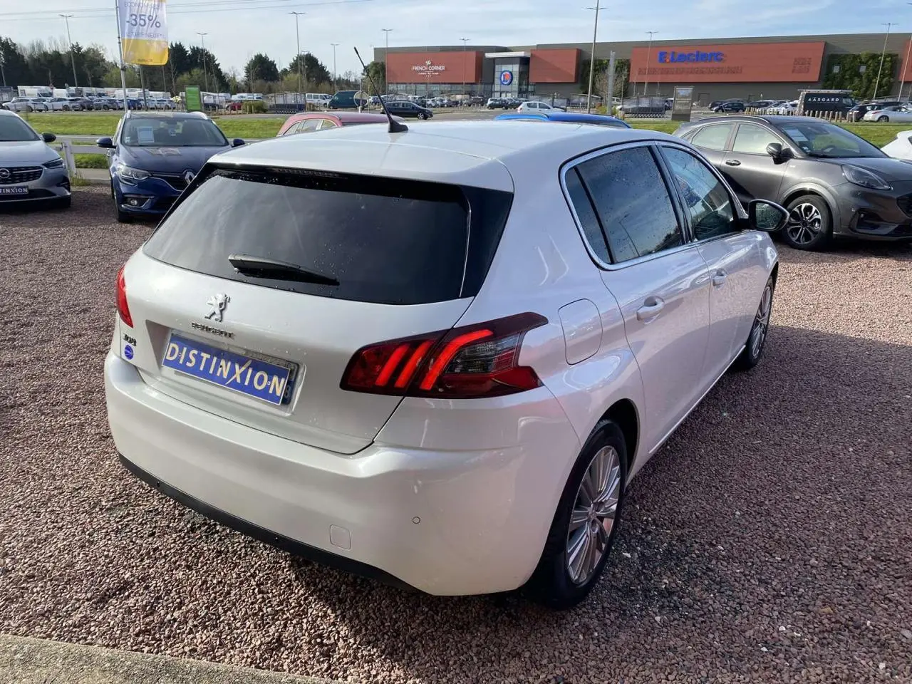 Peugeot 308 blanc nacré vue 3/4 arrière droit, vitres surteintées et feux arrière caractéristiques visibles.