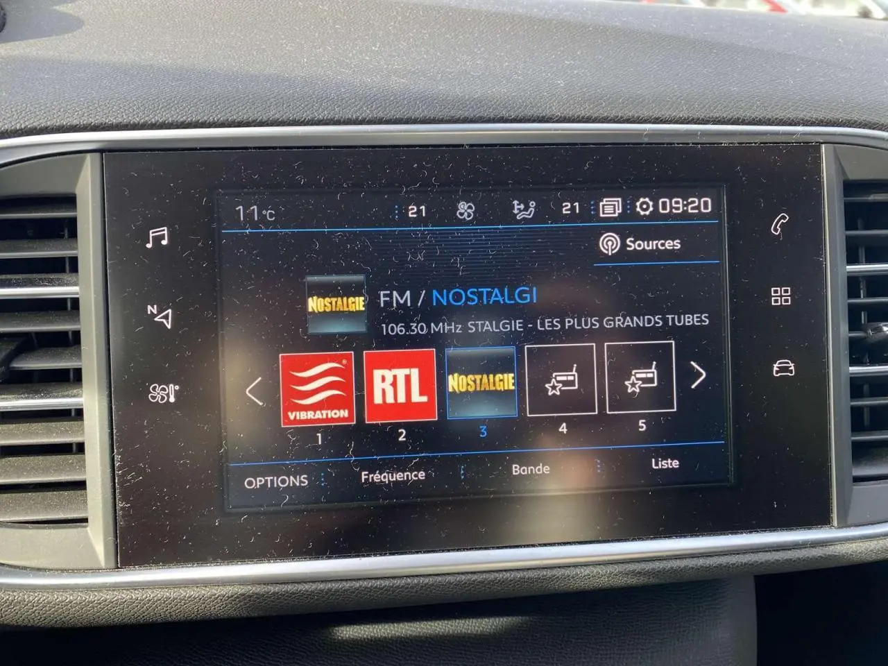 Écran tactile 9,7 pouces du tableau de bord d'une Peugeot 308 blanche, affichant les radios FM avec interface connectée.