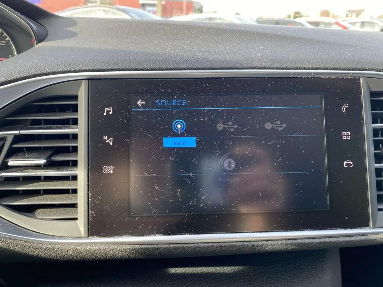 Écran tactile central allumé montrant les sources audio dans l'habitacle d'une Peugeot 308 blanche de 2017.