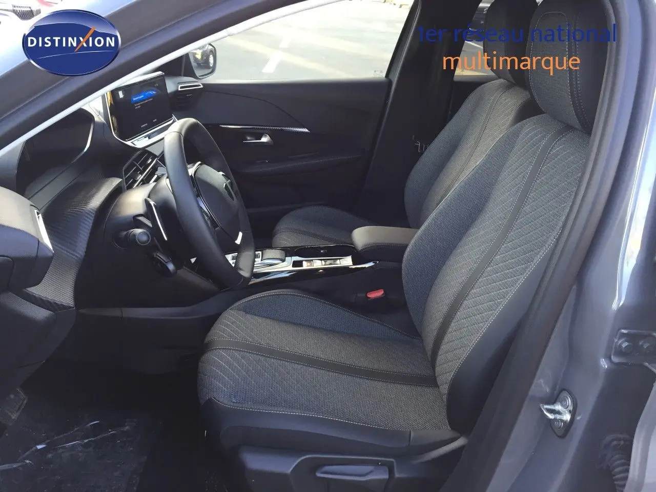 Intérieur avant droit du Peugeot 208 gris Selenium, sièges tissu noir avec console centrale et volant visible.