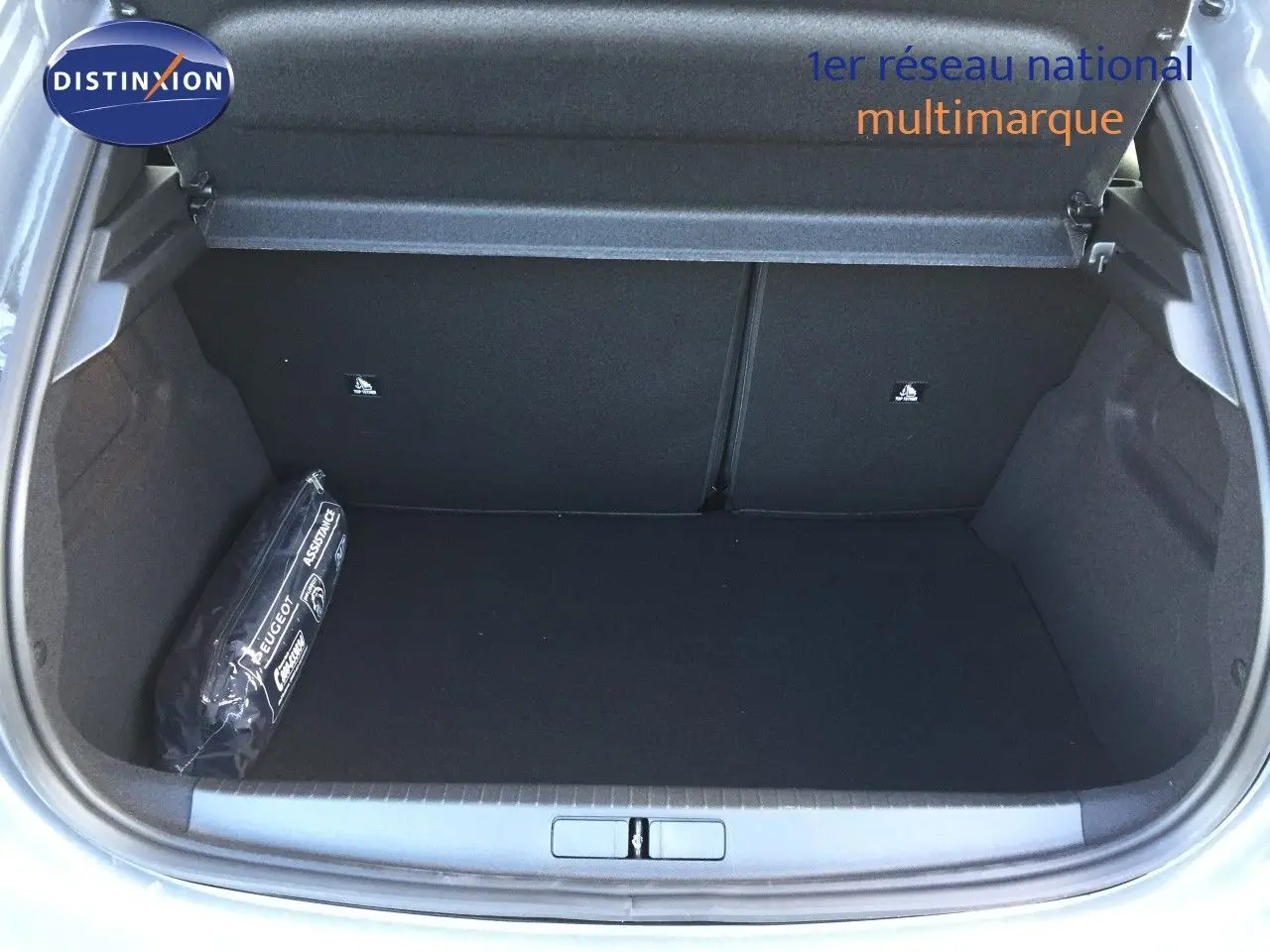 Coffre ouvert d'une Peugeot 208 gris selenium metal, montrant un espace de rangement vide avec une trousse d'assistance sur la gauche.