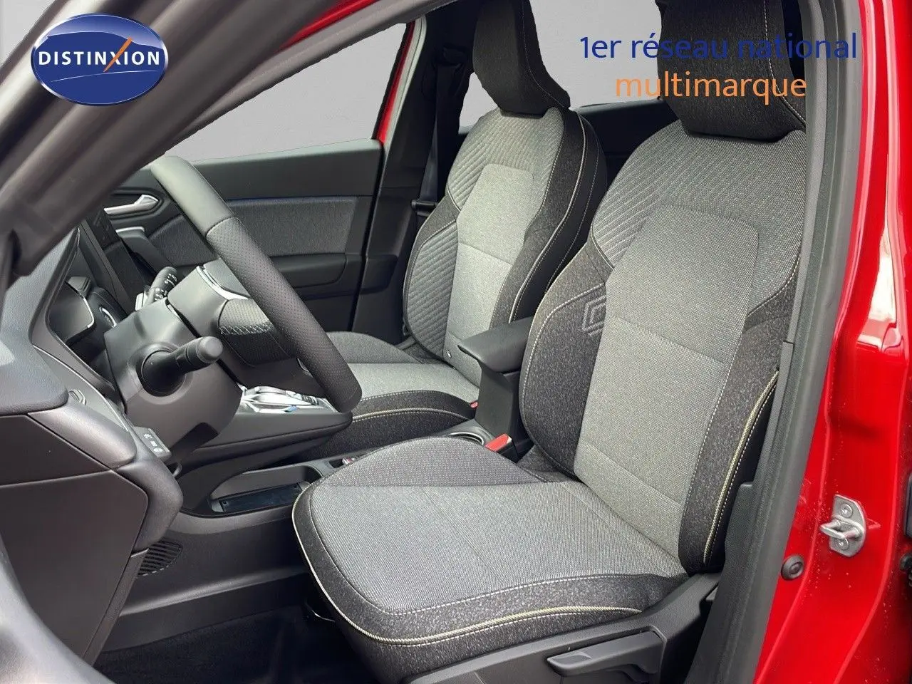Vue intérieure côté conducteur du Renault Captur E-Tech rouge passion, montrant les sièges tissu gris et noir avec coutures contrastées.