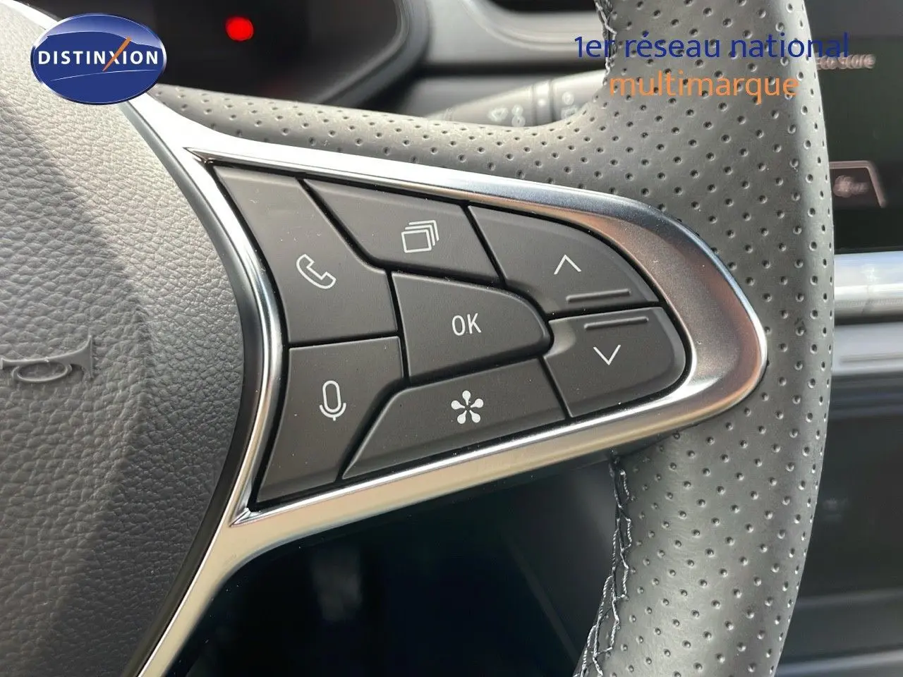 Gros plan sur les commandes multifonctions à gauche du volant perforé du Renault Captur rouge passion 2025.