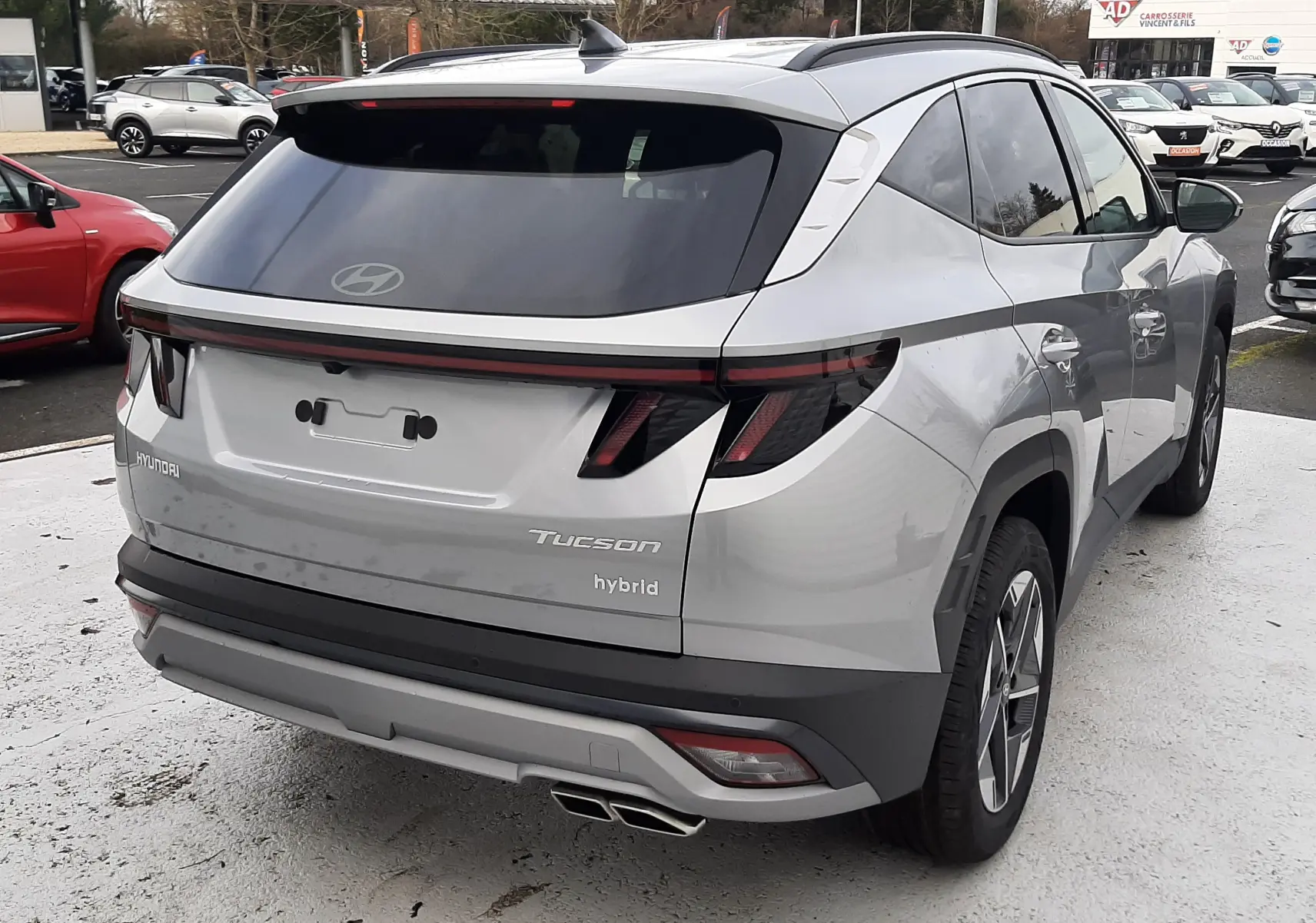 Vue 3/4 arrière droite d'un Hyundai Tucson gris Shimmering Silver hybride, avec feux arrière LED et double sortie d'échappement.