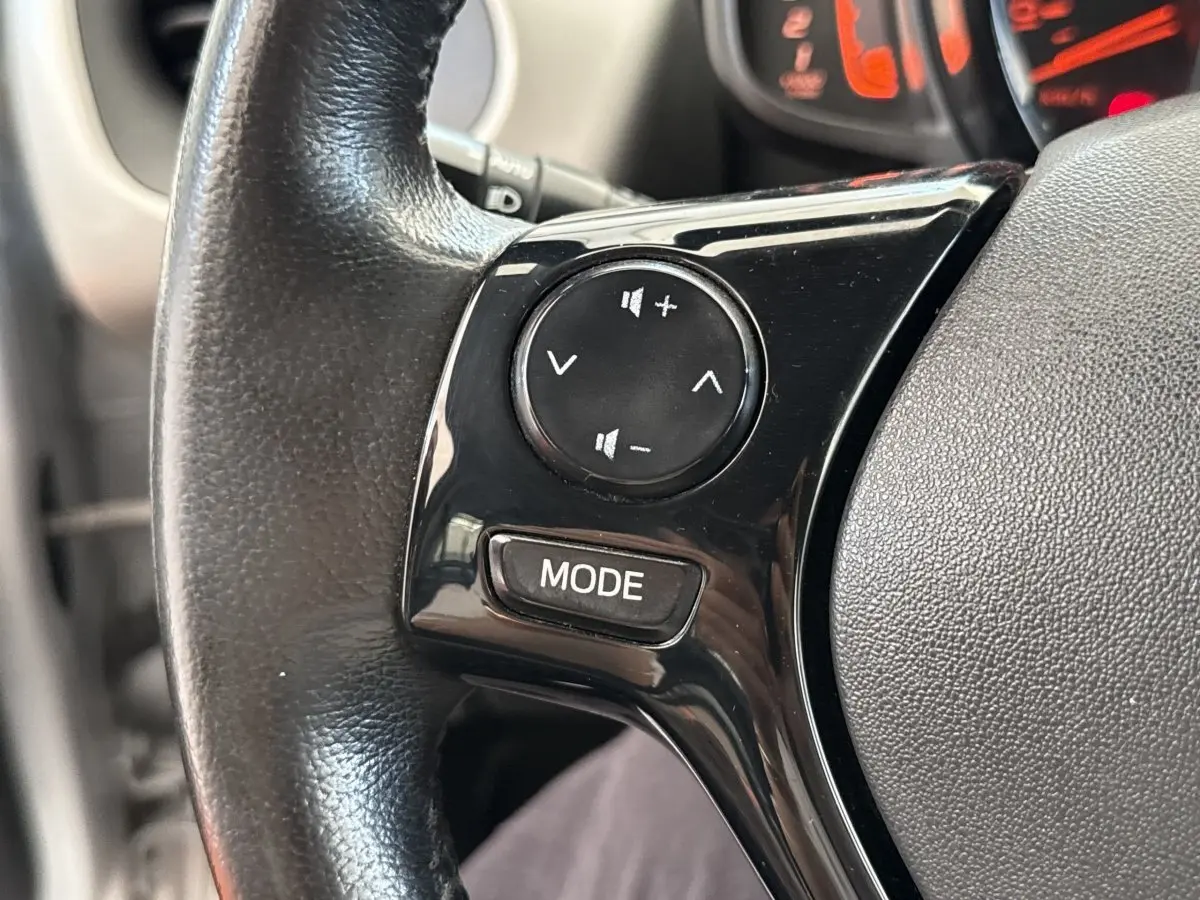 Gros plan sur le volant noir de la Toyota Aygo 2017, avec commandes audio intégrées et tableau de bord en arrière-plan.