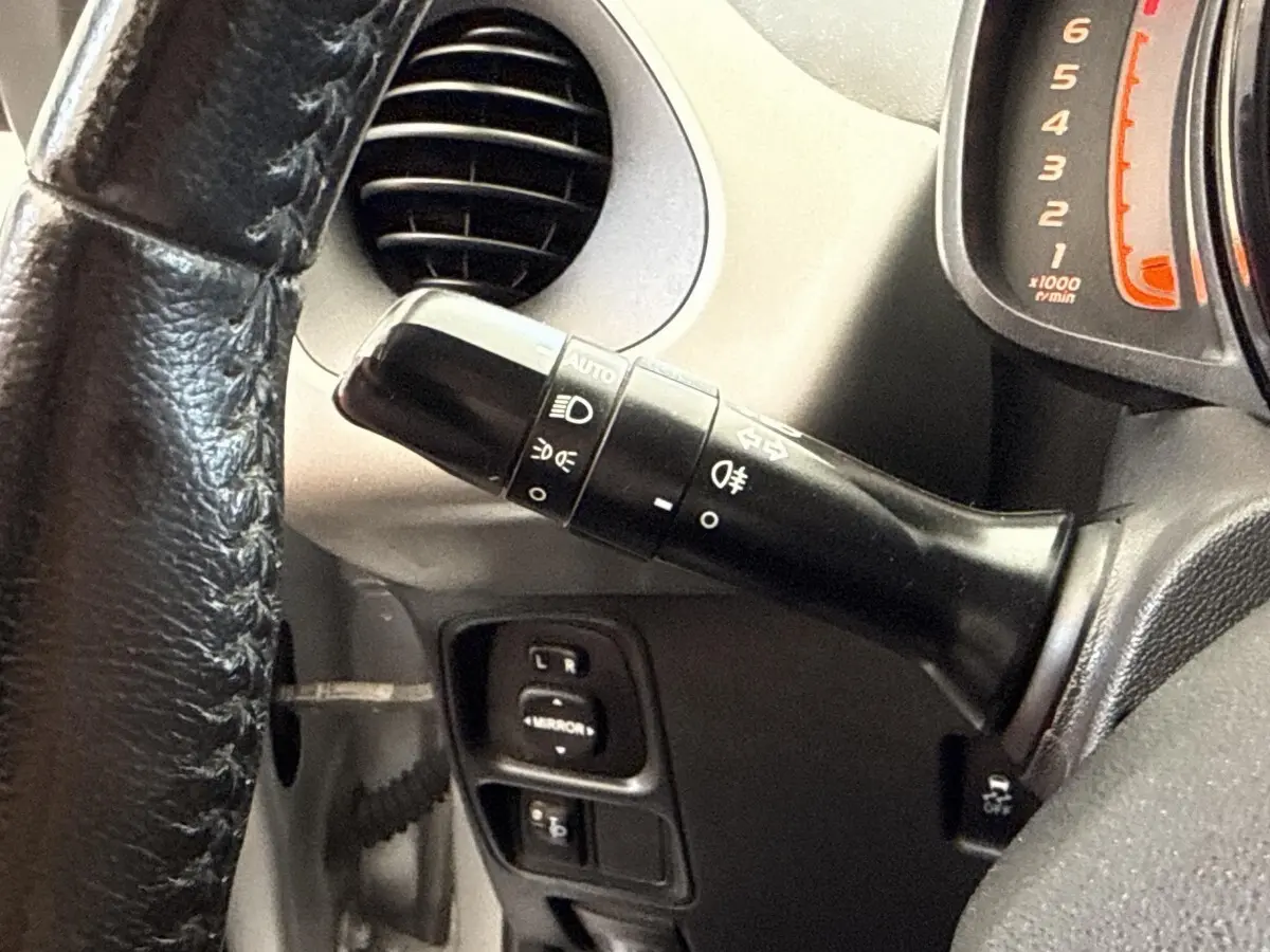 Gros plan sur la commande des phares et clignotants à gauche du volant d'une Toyota Aygo gris clair, tableau de bord partiel visible.