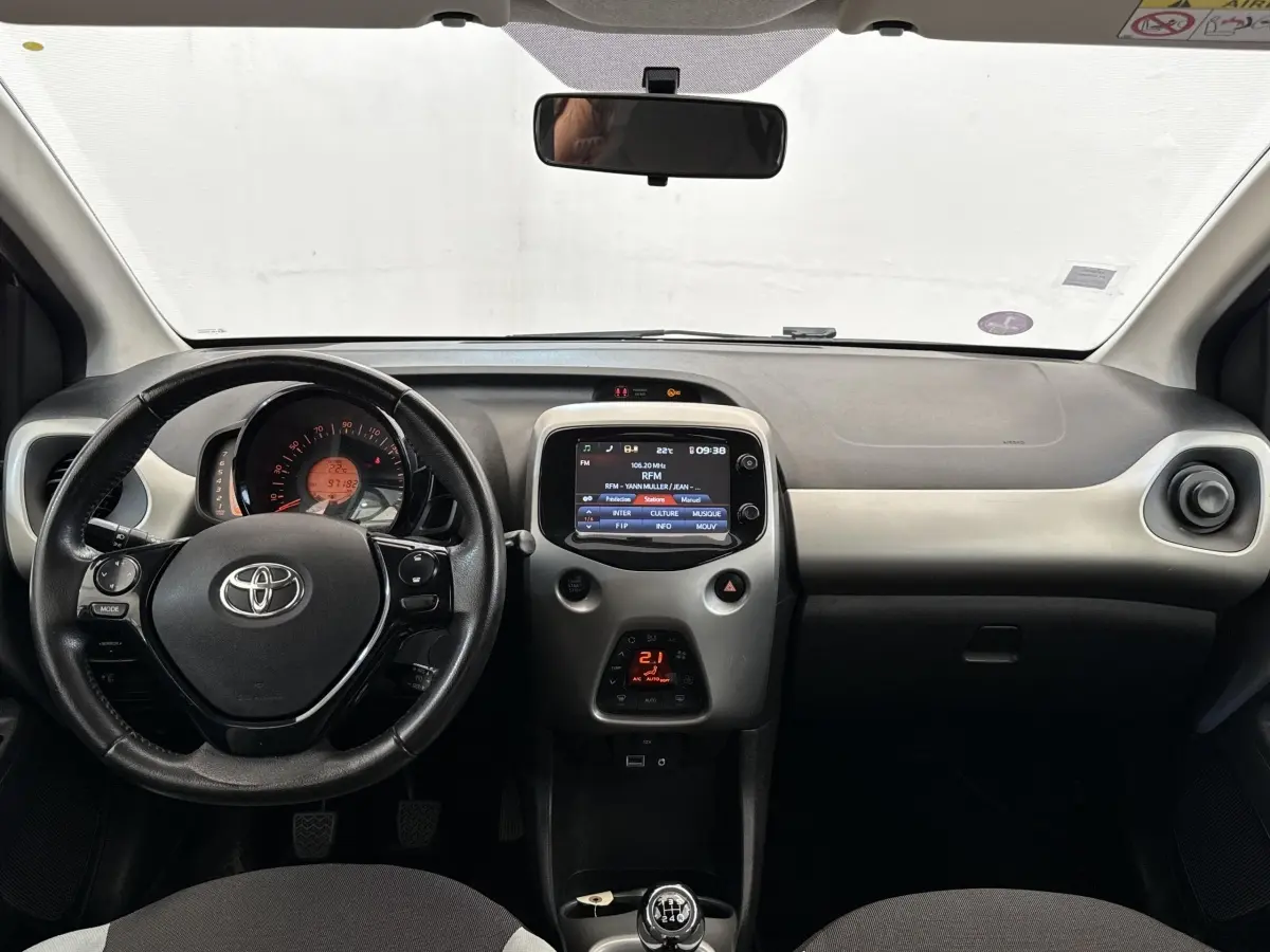 Vue intérieure frontale du tableau de bord gris clair et noir de la Toyota Aygo 2017 avec volant multifonction et écran tactile central.