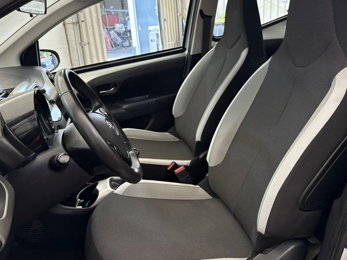 Vue intérieure côté conducteur de la Toyota Aygo 2017, sièges tissu gris clair et noir avec volant réglable.