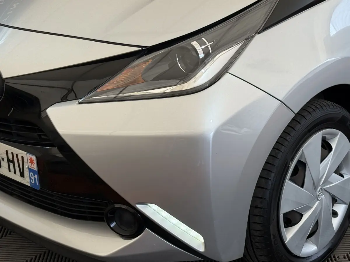 Gros plan sur l'avant droit gris clair de la Toyota Aygo 2017, mettant en valeur le phare et la roue.