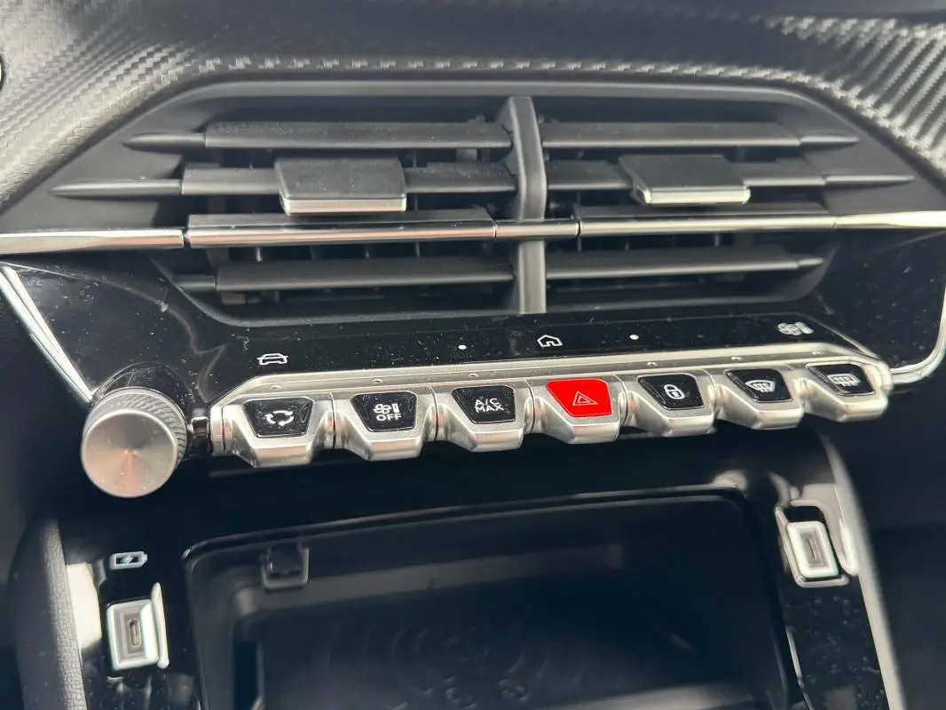 Gros plan sur la console centrale de la Peugeot 208 Hybrid 110 e-DCS6 GT 2025, boutons argentés et écran tactile noir.