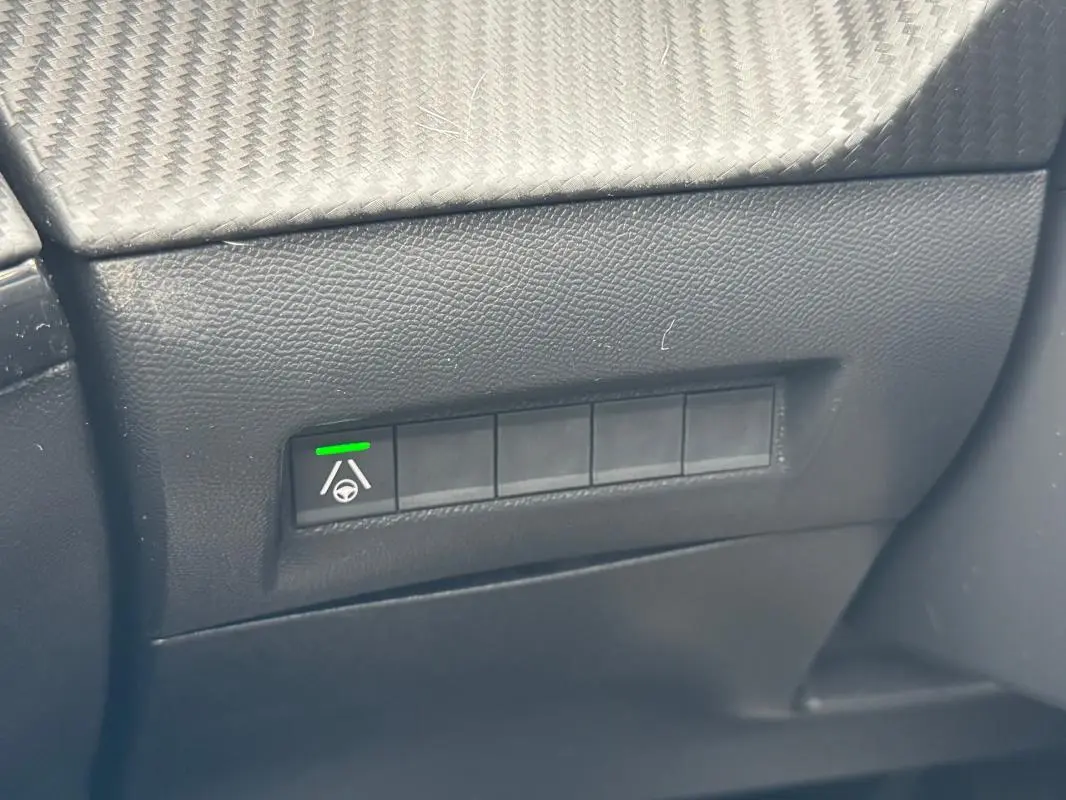 Gros plan sur le tableau de bord noir du Peugeot 208 Hybrid 110 e-DCS6 GT, montrant un bouton d’aide à la conduite activé.