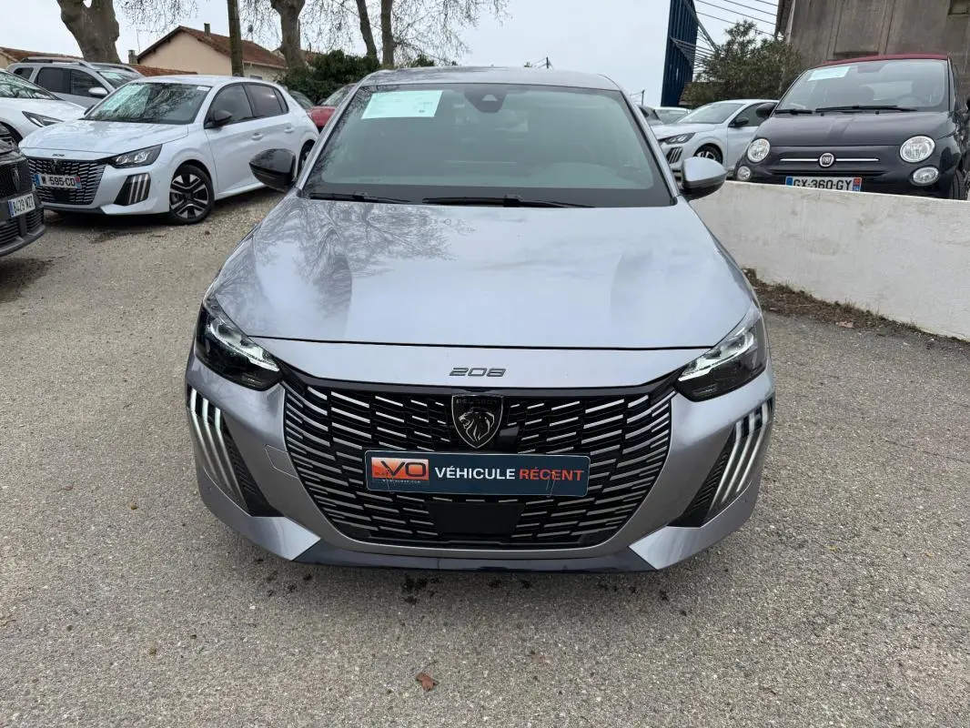 Vue frontale d'une Peugeot 208 gris clair 2025 avec calandre noire et feux LED distinctifs allumés.
