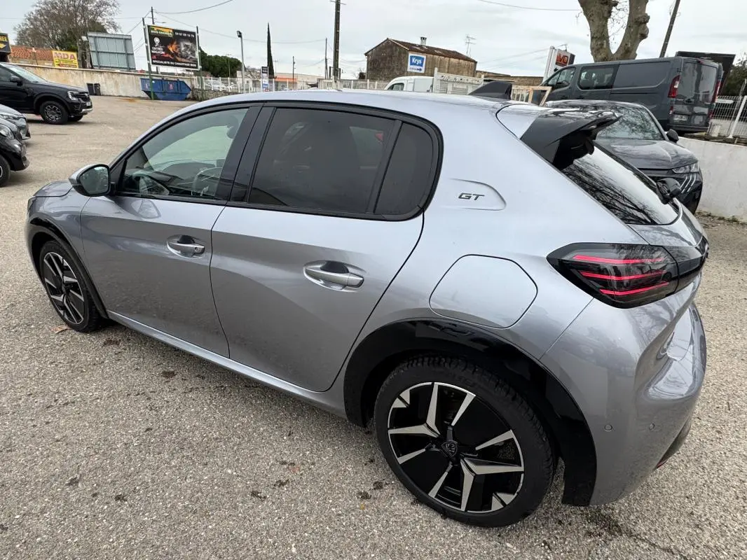 Vue 3/4 arrière droite d'une Peugeot 208 Hybrid 110 GT gris métallisé avec jantes alliage 17 pouces et logo GT sur l'aile.
