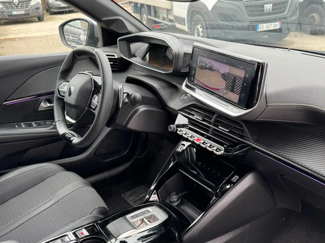 Vue intérieure côté conducteur du Peugeot 208 Hybrid 110 e-DCS6 GT 2025, avec tableau de bord moderne et écran tactile affichant la caméra de recul.